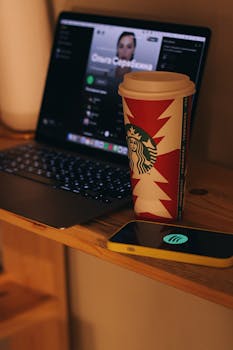 pexels photo 14704463 14704463 A Starbucks coffee cup beside a laptop and smartphone in a cozy indoor setting.